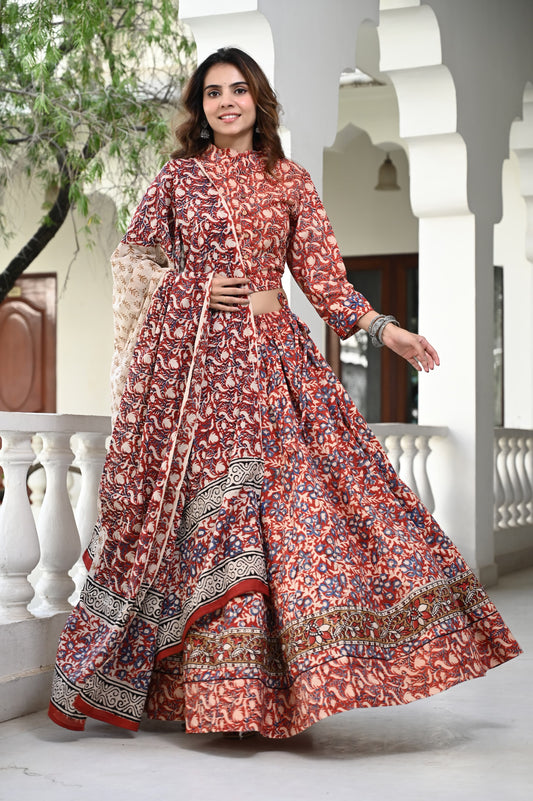 A woman wearing a traditional maroon lehenga set with block printed designs and a crop top, standing on a balcony.