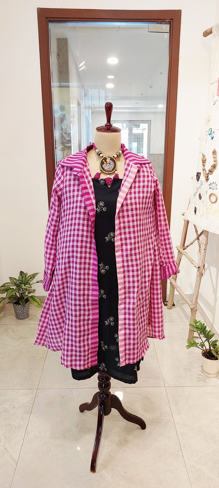 S long magenta and white checkered Gamcha shrug over a black floral embroidered midi dress with a statement tribal necklace.