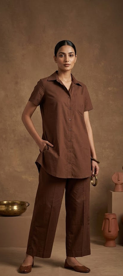 Woman in a brown outfit standing against a brown background with decorative vases.